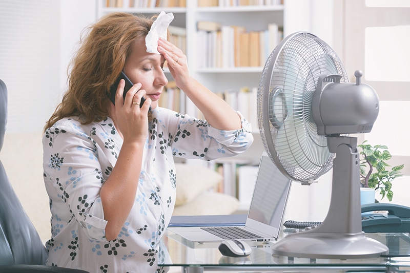 Woman trying to cool off in front of fan, due to air conditioning not cooling home. Scott Brothers Heating & Air blog image.