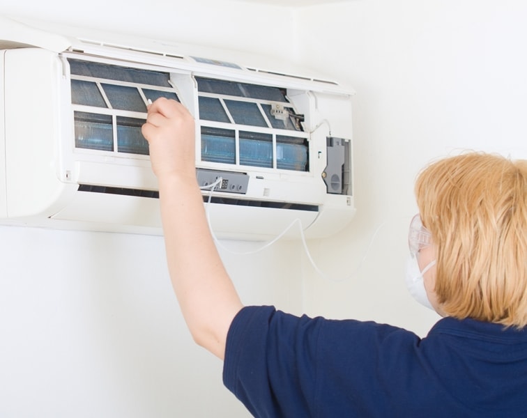 Woman cleaning dirty ductless air conditioner with spray.