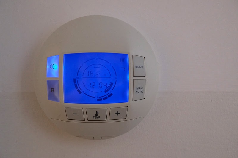 How to Set Your Programmable Thermostat. Photo of a digital thermostat mounted on a wall with blue lights.